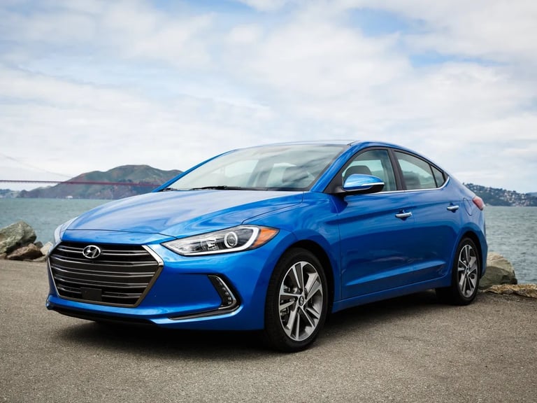 Blue Hyundai Elantra sedan parked on a beach overlook with water and hills in the background