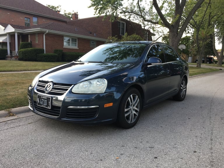 Dark blue Volkswagen Jetta sedan parked in a residential driveway on a tree-lined street